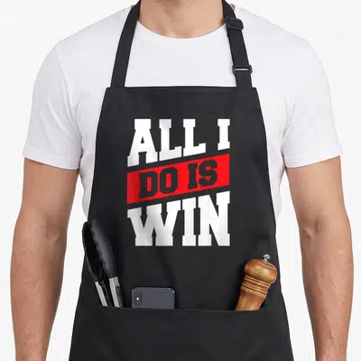 Win urban apron - Stacked white and grey text reading All I Do Is Win inside a red slanted bar on black fabric — shown on a black cotton canvas apron against a white background