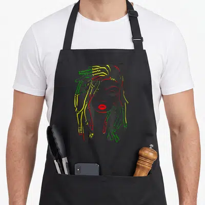 Rasta hair color apron - Cartoon woman with grey skin and dreadlocks outlined in yellow green and red — shown on a black cotton canvas apron against a white background