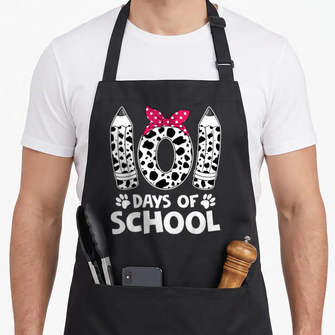 Vintage school teacher apron - Number 100 made of cow-print pencils and pink bow with DAYS OF SCHOOL text and paw — shown on a black cotton canvas apron against a white background