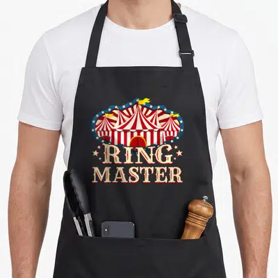 Ringmaster circus apron - Striped circus tent in blue scalloped frame above stacked RING MASTER text flanked by stars — shown on a black cotton canvas apron against a white background