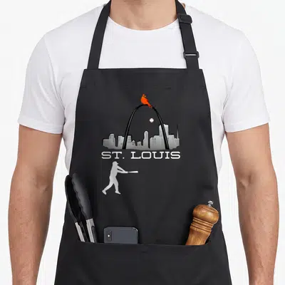 Player cardinal apron - St. Louis skyline with red cardinal on arch and white baseball batter silhouette below text — shown on a black cotton canvas apron against a white background