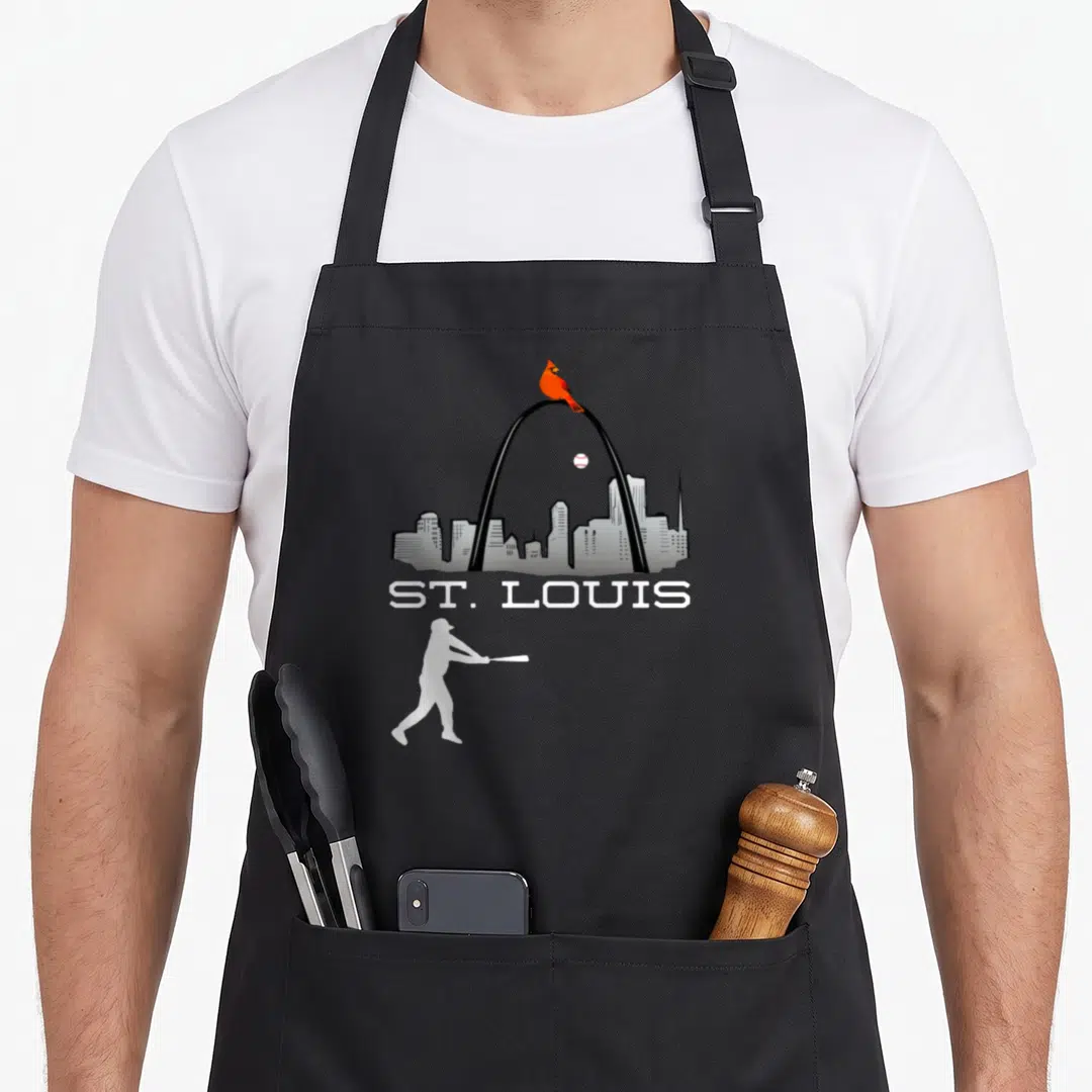 Player cardinal apron - St. Louis skyline with red cardinal on arch and white baseball batter silhouette below text — shown on a black cotton canvas apron against a white background