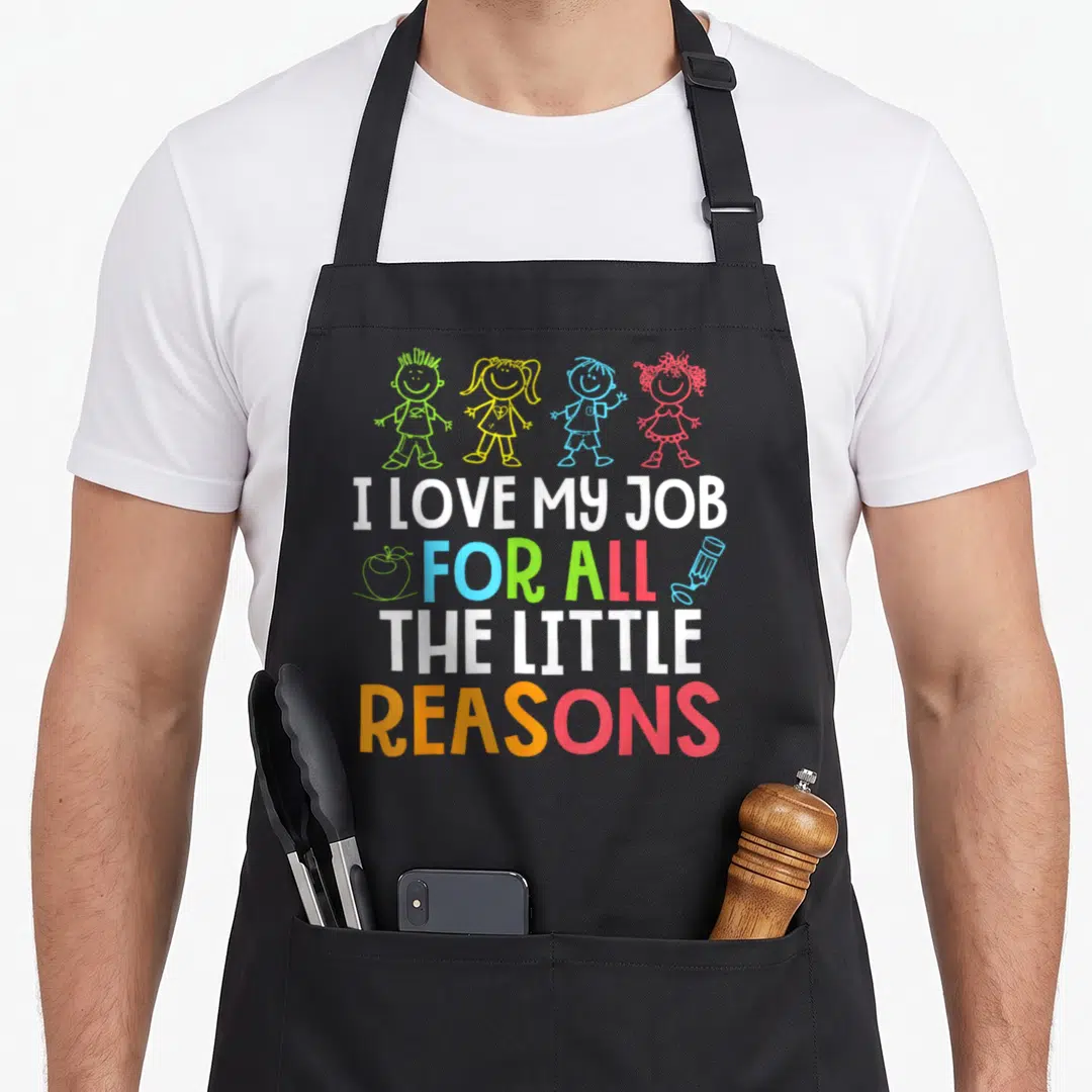 Cute reason teacher apron - Four cartoon children above I LOVE MY JOB FOR ALL THE LITTLE REASONS text with apple — shown on a black cotton canvas apron against a white background