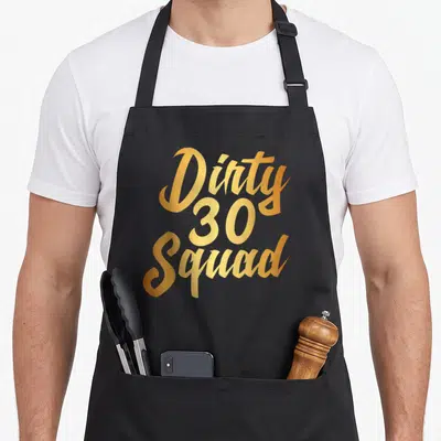 Thirty squad funny dirty aprons - Gold script text Dirty 30 Squad stacked vertically — shown on a black cotton canvas apron against a white background