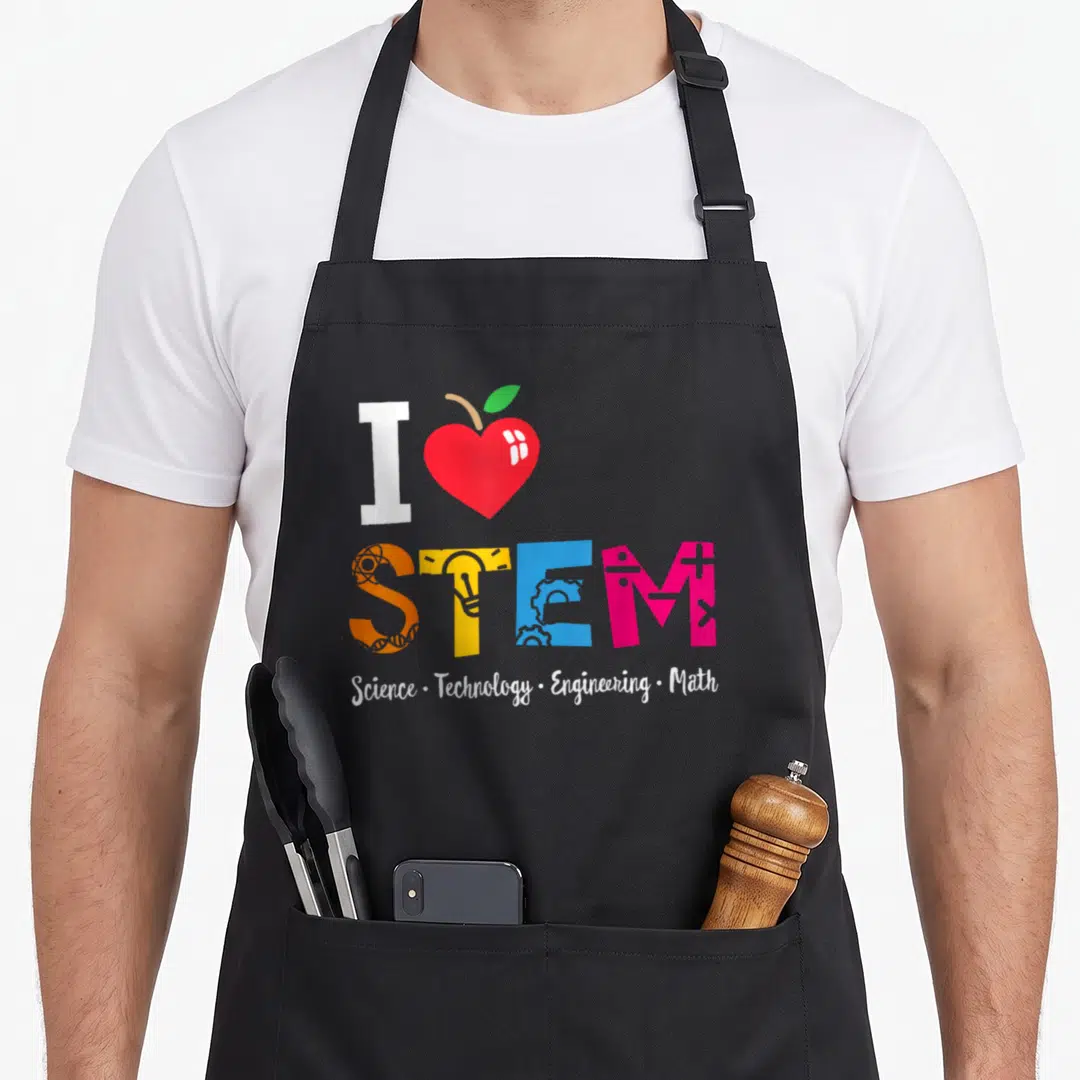 Outside box teacher apron - I heart STEM acronym with atomic gear lightbulb math symbols and full subject list below — shown on a black cotton canvas apron against a white background
