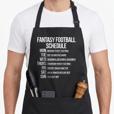 Schedule football apron - White stacked text listing fantasy football tasks like waiver claims and research for each — shown on a black cotton canvas apron against a white background