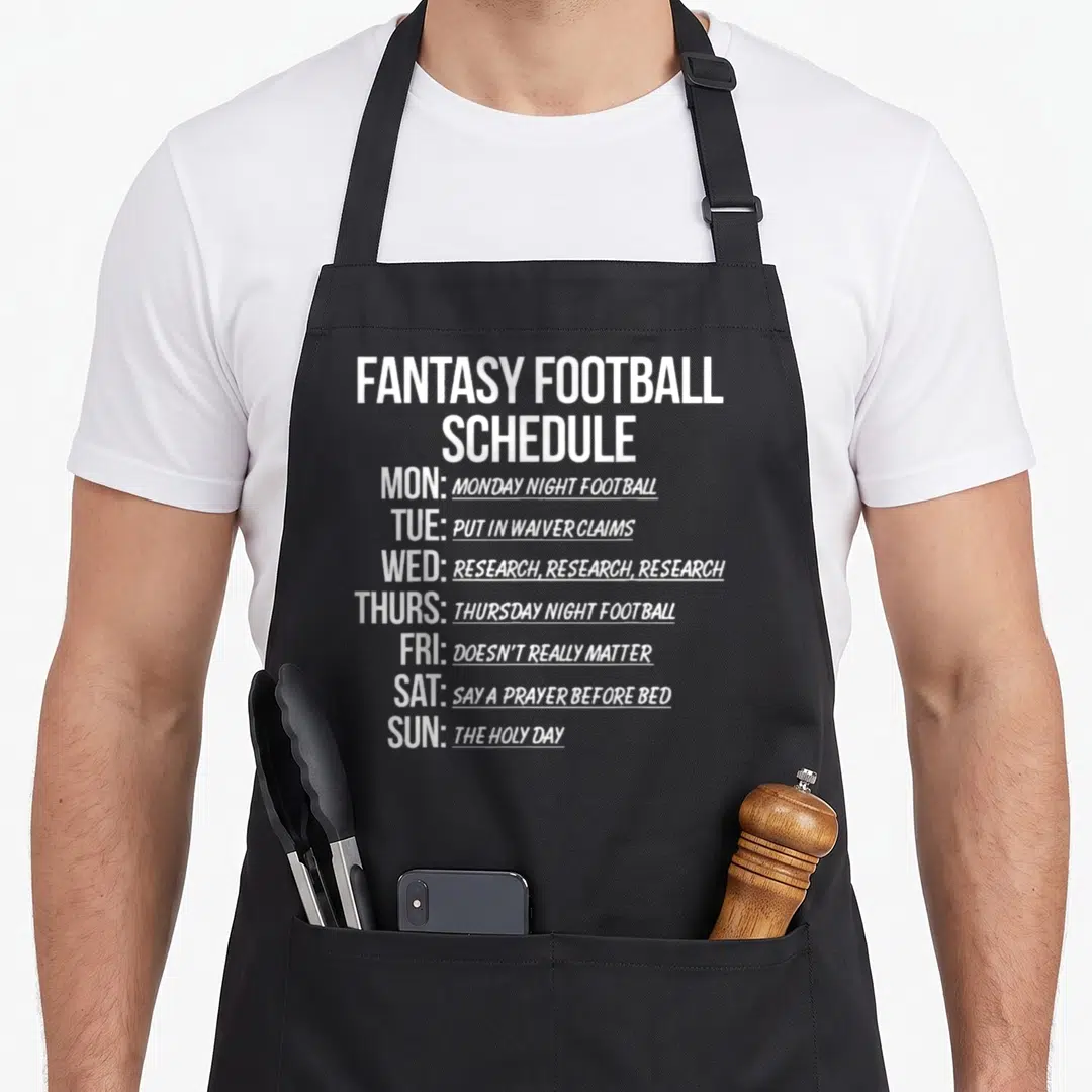 Schedule football apron - White stacked text listing fantasy football tasks like waiver claims and research for each — shown on a black cotton canvas apron against a white background