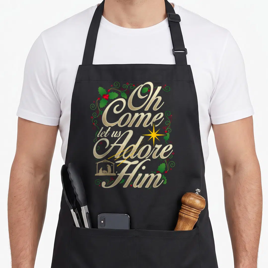 Come christmas apron - Stacked gold text Oh Come Let Us Adore Him with holly and nativity manger silhouette — shown on a black cotton canvas apron against a white background