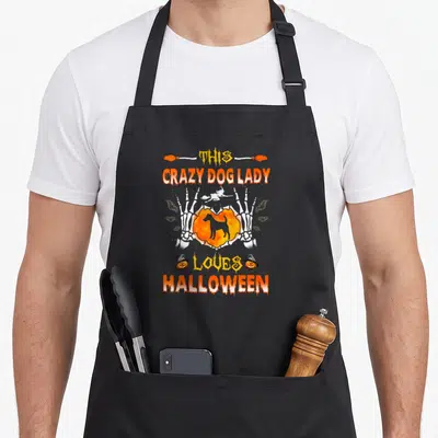 Smooth fox dog apron - Skeleton hands hold orange heart with black dog silhouette beneath witch on broom, surrounded — shown on a black cotton canvas apron against a white background