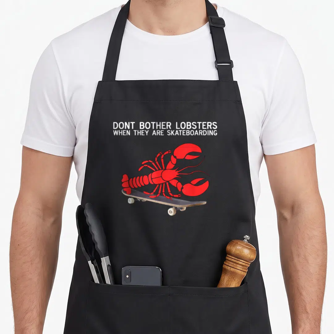 Skateboarding lobster apron - Red lobster standing on skateboard below white text DONT BOTHER LOBSTERS WHEN THEY ARE — shown on a black cotton canvas apron against a white background