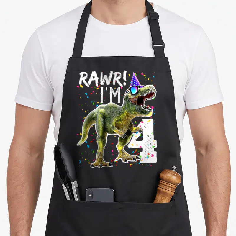 Rawr t rex apron - T-Rex in party hat and sunglasses next to white number 4 with confetti — shown on a black cotton canvas apron against a white background