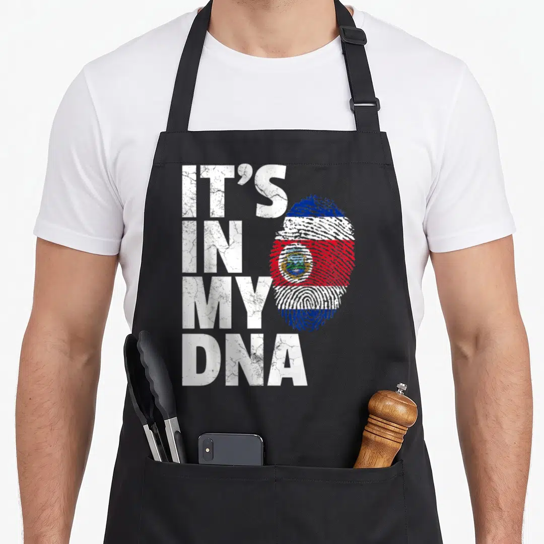 Costa pride apron - Stacked IT'S IN MY DNA text next to a distressed fingerprint flag in white blue and red — shown on a black cotton canvas apron against a white background