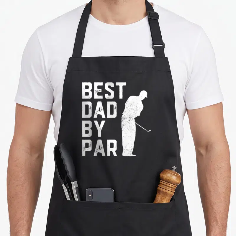 Golf father day apron - White distressed text Best Dad By Par beside a golfer silhouette putting on black fabric — shown on a black cotton canvas apron against a white background