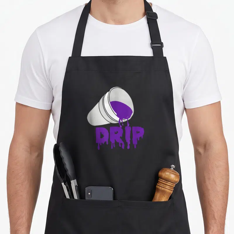 Codeine hip apron - Tilted white cup pouring purple liquid forming the word DRIP in cartoon style — shown on a black cotton canvas apron against a white background
