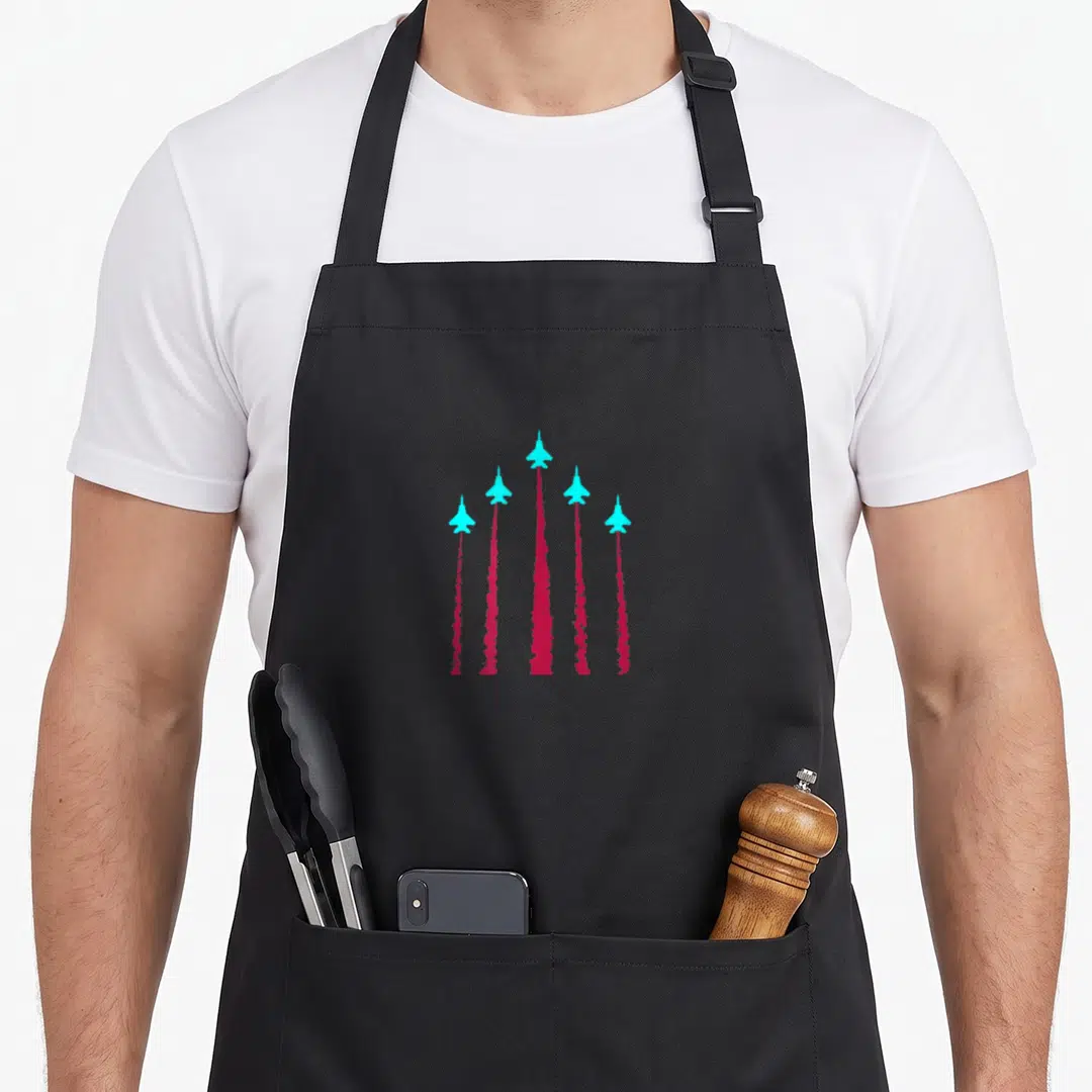 Jet airplane apron - Five cyan jets in V-formation with red smoke trails on gray background — shown on a black cotton canvas apron against a white background