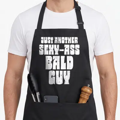Bald father day apron - White stacked text reading JUST ANOTHER SEXY-ASS BALD GUY with distressed texture — shown on a black cotton canvas apron against a white background