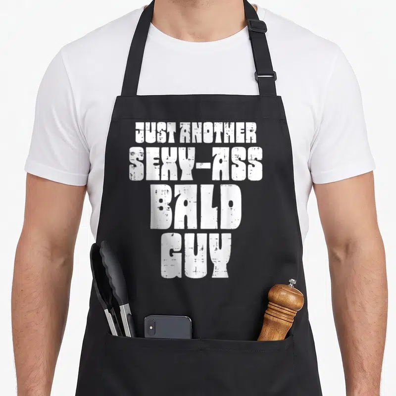 Bald father day apron - White stacked text reading JUST ANOTHER SEXY-ASS BALD GUY with distressed texture — shown on a black cotton canvas apron against a white background