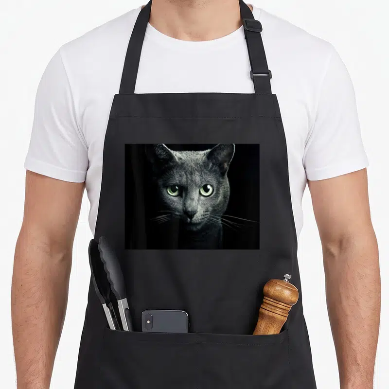 Cat russian aprons - Photographic portrait of a grey cat face with green eyes on a black background — shown on a black cotton canvas apron against a white background