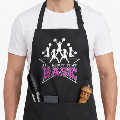 Base cheerleading apron - Five white cheerleader silhouettes above pink and white ALL ABOUT THAT BASE text — shown on a black cotton canvas apron against a white background