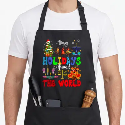 Vacation xmas apron - Cartoon Christmas tree, dancers, menorah, lanterns, lion dance head, and stacked colorful text — shown on a black cotton canvas apron against a white background