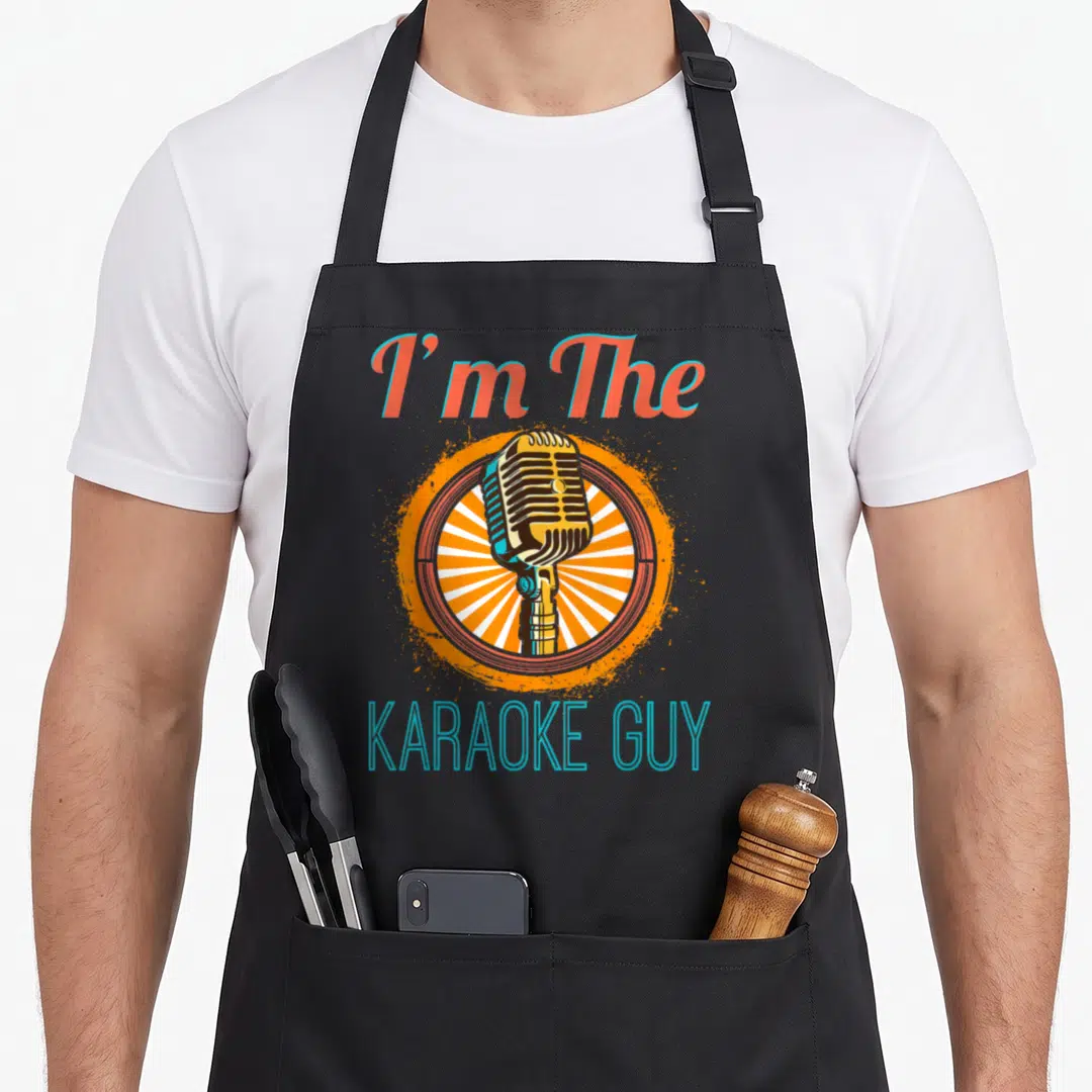 Singer karaoke apron - Vintage microphone in orange circle with white sunburst and text I'm The KARAOKE GUY — shown on a black cotton canvas apron against a white background