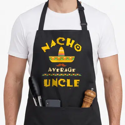 Uncle mexican apron - Nacho Average Uncle text above a striped sombrero and brown mustache in yellow and green — shown on a black cotton canvas apron against a white background