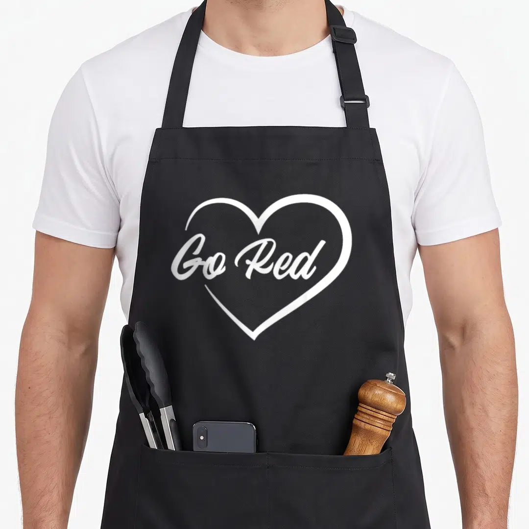 Month heart disease awareness apron - White heart outline containing Go Red cursive text on dark background — shown on a black cotton canvas apron against a white background