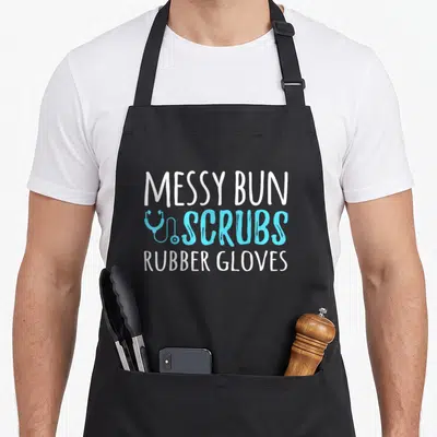 Messy rubber gloves and apron - Stacked white and blue text reading Messy Bun Scrubs Rubber Gloves next — shown on a black cotton canvas apron against a white background