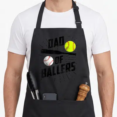 Baller softball baseball apron - DAD OF BALLERS text with bat, yellow softball, and white baseball in distressed style — shown on a black cotton canvas apron against a white background