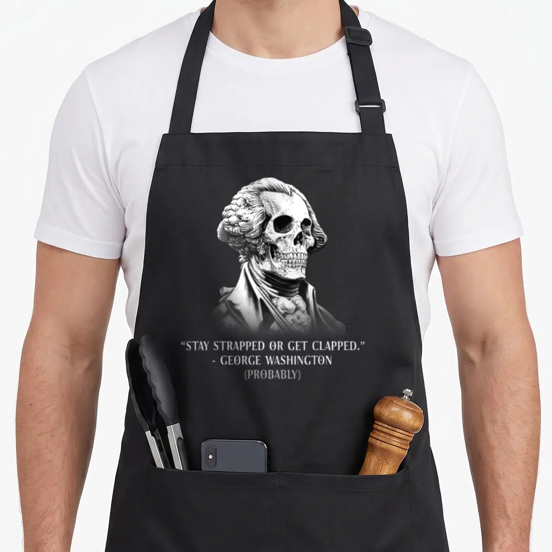 Stay apron or apron - Skeleton in colonial wig with Stay Strapped Or Get Clapped quote — shown on a black cotton canvas apron against a white background