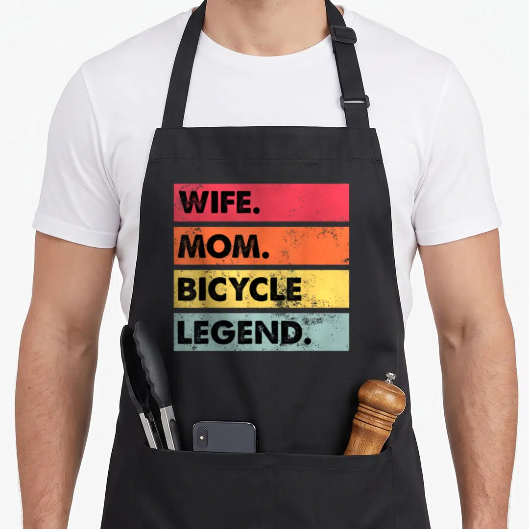 Bicycle mother's apron - Four horizontal bars in red orange yellow light blue with black text WIFE MOM BICYCLE LEGEND — shown on a black cotton canvas apron against a white background