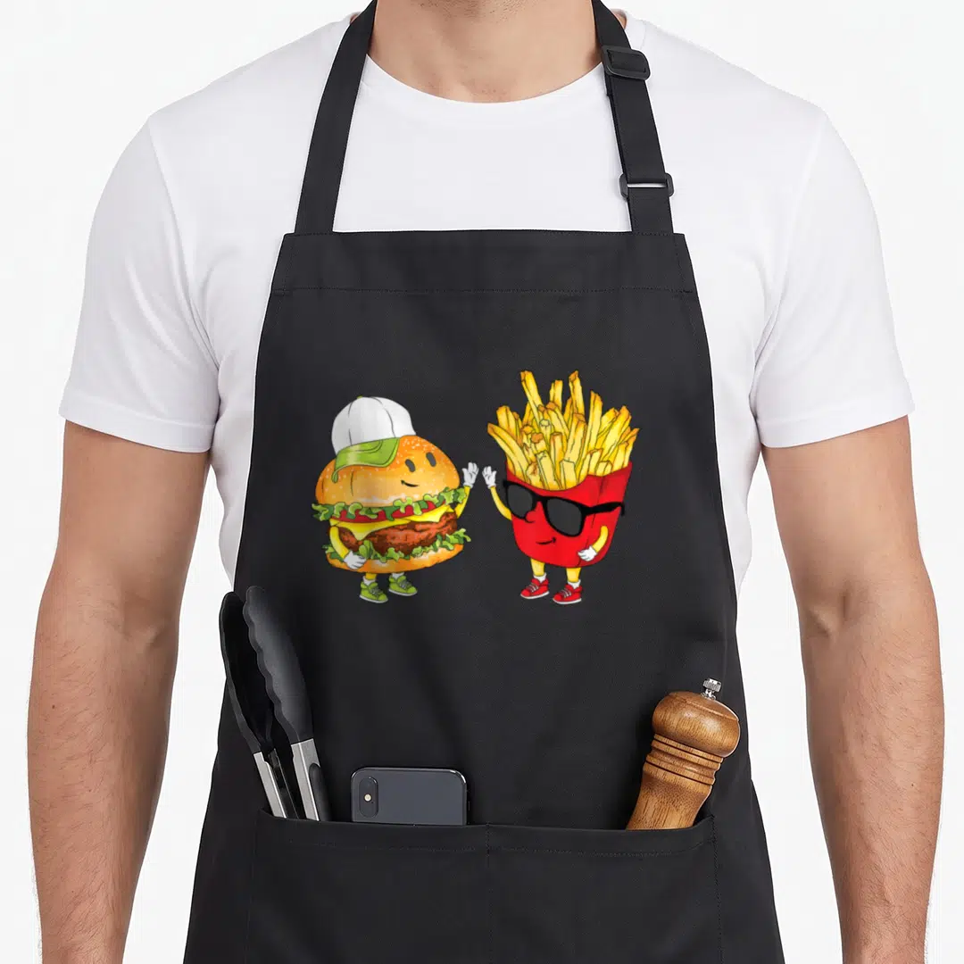 Hamburger fast food apron - Cartoon burger and fries high-fiving in yellow red green and brown — shown on a black cotton canvas apron against a white background