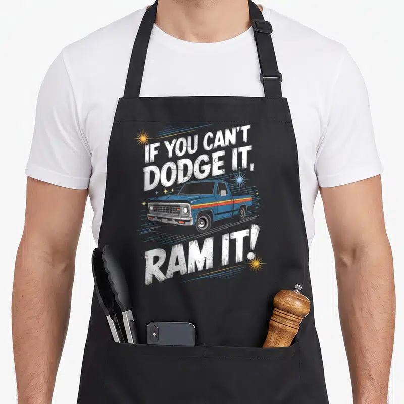 Pick ram apron - Blue vintage truck with IF YOU CAN'T DODGE IT RAM IT text and distressed stars — shown on a black cotton canvas apron against a white background