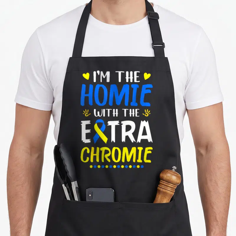 Homie an extra apron - Stacked blue yellow white text reading I'm the Homie with the Extra Chromie with ribbon — shown on a black cotton canvas apron against a white background