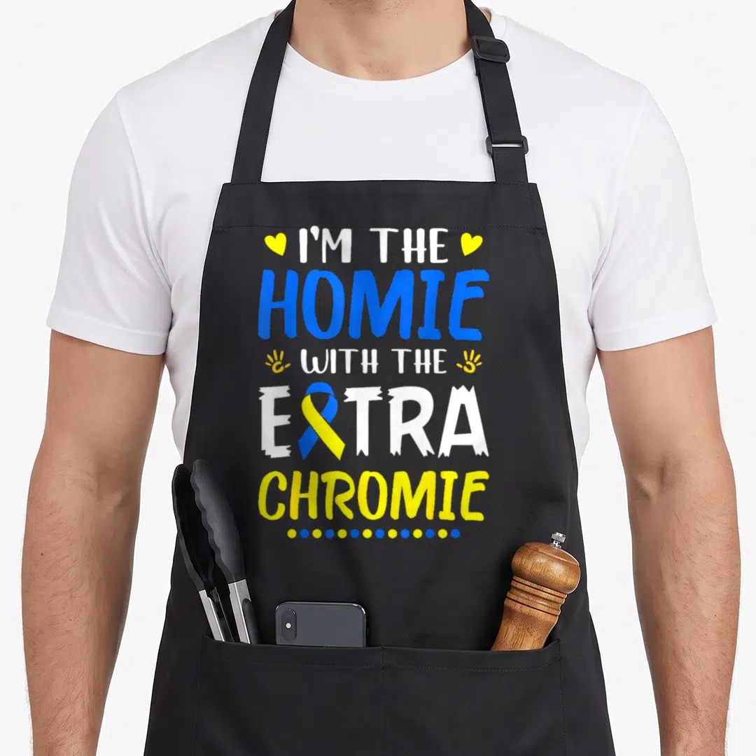 Homie an extra apron - Stacked blue yellow white text reading I'm the Homie with the Extra Chromie with ribbon — shown on a black cotton canvas apron against a white background