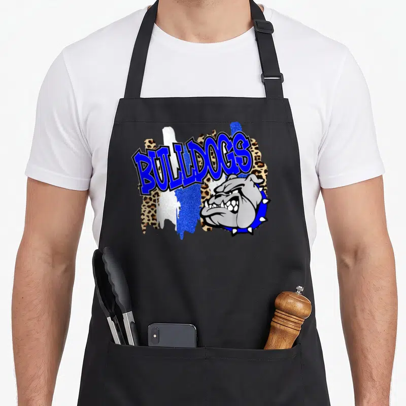 Funny bulldog school apron - Arched blue BULLDOGS text above a grey bulldog head with leopard and glitter splashes — shown on a black cotton canvas apron against a white background