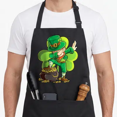 Dance st patrick day aprons - Cartoon leprechaun dabbing pose standing on a pot of gold coins in green and brown — shown on a black cotton canvas apron against a white background