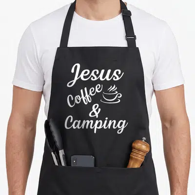 Jesus camping apron - White stacked text Jesus Coffee & Camping with small steaming cup icon beside Coffee — shown on a black cotton canvas apron against a white background