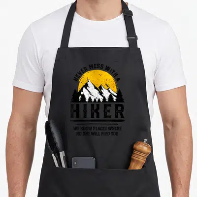 Hiker outdoor apron - Retro mountain graphic with Never Mess With A Hiker quote in black yellow and white — shown on a black cotton canvas apron against a white background