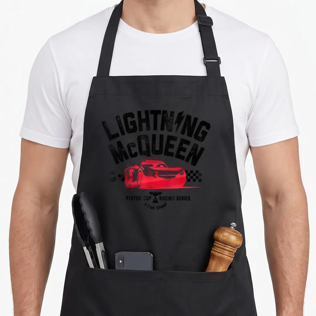 Piston car apron - Lightning McQueen red race car with Piston Cup Racing Series text and trophy — shown on a black cotton canvas apron against a white background
