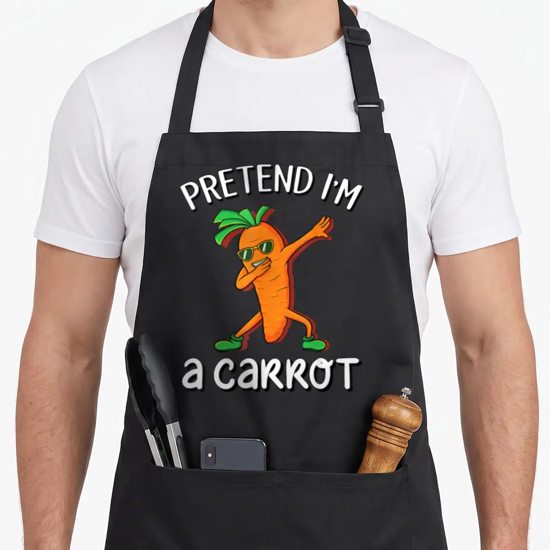 Vegan halloween apron - Orange cartoon carrot dabbing with sunglasses between Pretend I'm a Carrot text — shown on a black cotton canvas apron against a white background