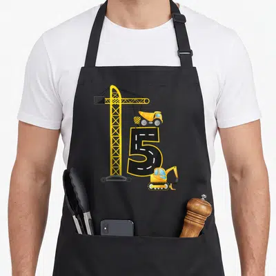 Construction vehicle truck apron - Yellow crane lifting dump truck over black number 5 road design with excavator — shown on a black cotton canvas apron against a white background