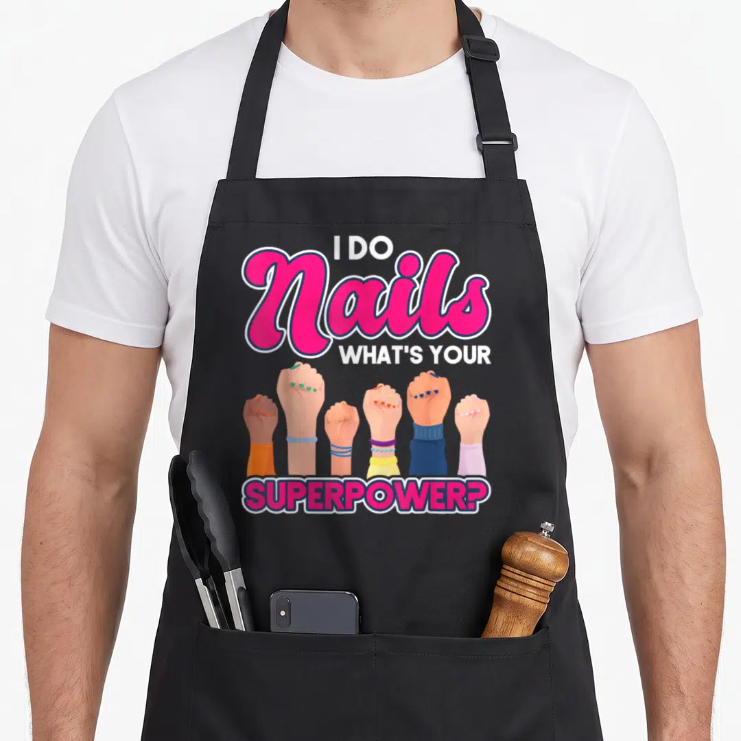 Nail artist manicurist apron - I DO Nails text above six raised fists with painted nails in pink and blue — shown on a black cotton canvas apron against a white background