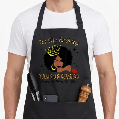 Birthday queen taurus aprons - Cartoon woman with afro and crown, It's My Birthday Taurus Queen text, leopard print — shown on a black cotton canvas apron against a white background