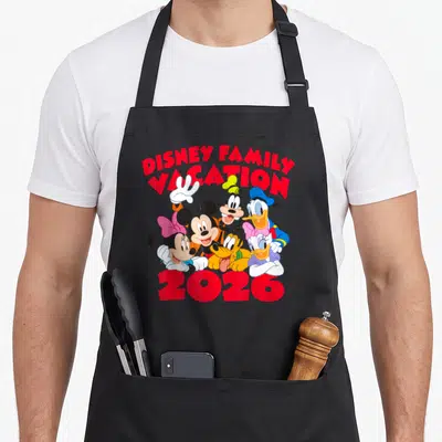 Family vacation friends apron - Red DISNEY FAMILY VACATION 2026 text above a cluster of Mickey, Minnie, Goofy, Donald — shown on a black cotton canvas apron against a white background
