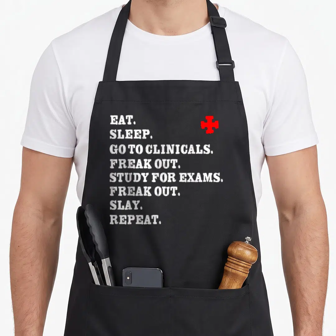 Slay nurse apron - White stacked text EAT SLEEP GO TO CLINICALS with red cross symbol — shown on a black cotton canvas apron against a white background