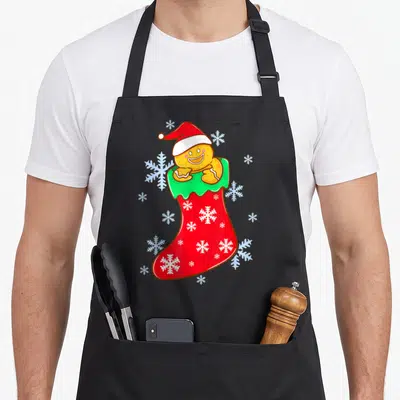 Stocking christmas gingerbread apron - Cartoon gingerbread man in santa hat inside red stocking with white snowflakes — shown on a black cotton canvas apron against a white background