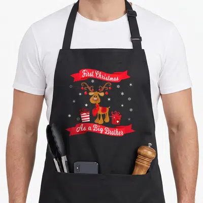 Brother christmas aprons - Cartoon reindeer with gifts and red ribbons reading First Christmas As a Big Brother — shown on a black cotton canvas apron against a white background