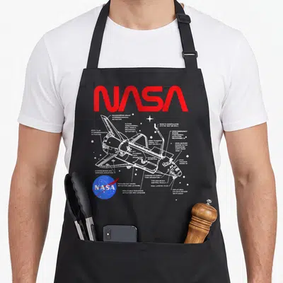 Space nasa apron - White space shuttle schematic with red NASA text and blue logo on black bib — shown on a black cotton canvas apron against a white background
