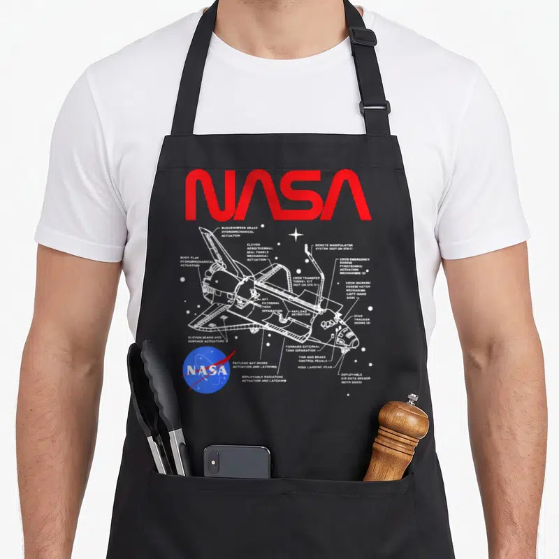 Space nasa apron - White space shuttle schematic with red NASA text and blue logo on black bib — shown on a black cotton canvas apron against a white background